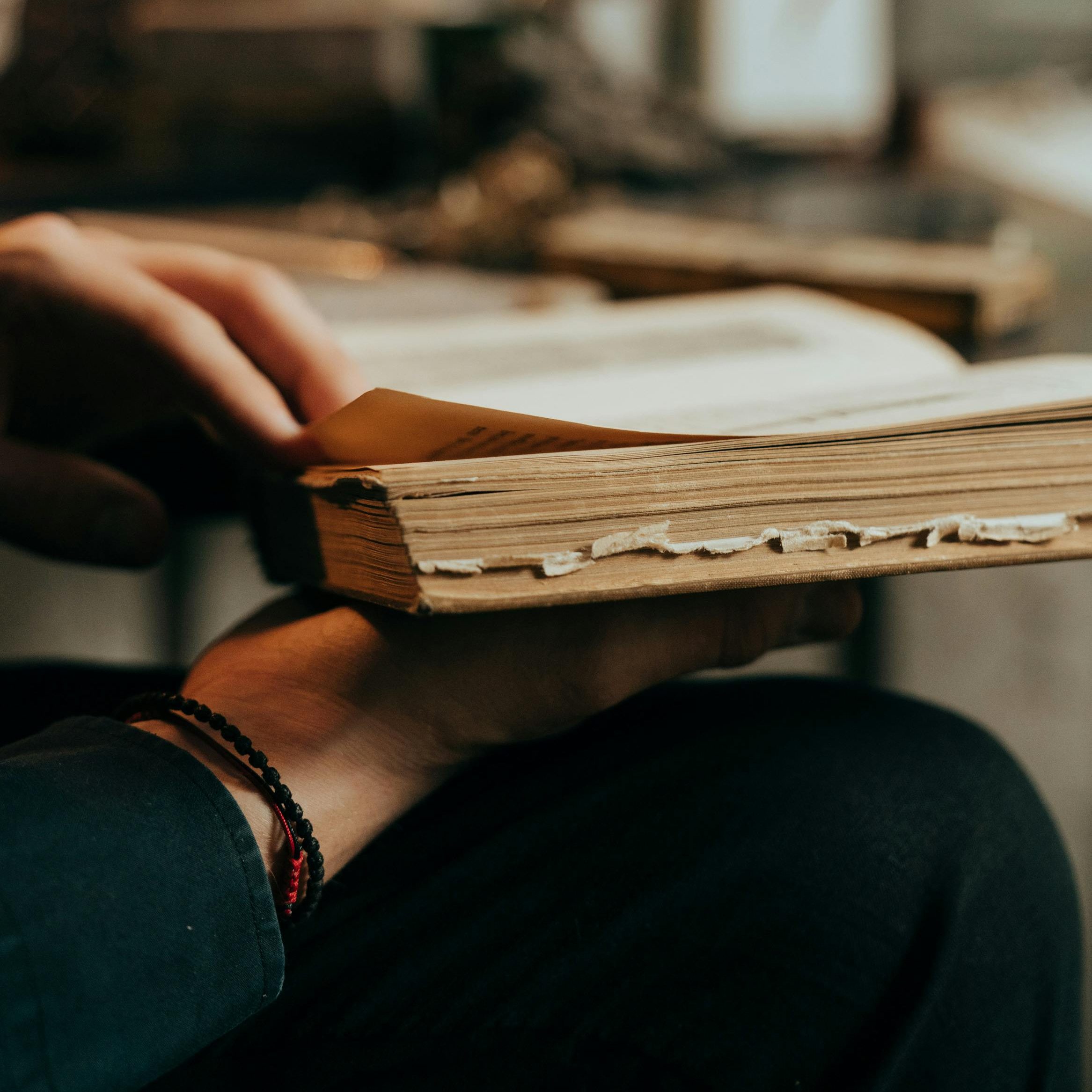 A man holding old books and about to turn a page.