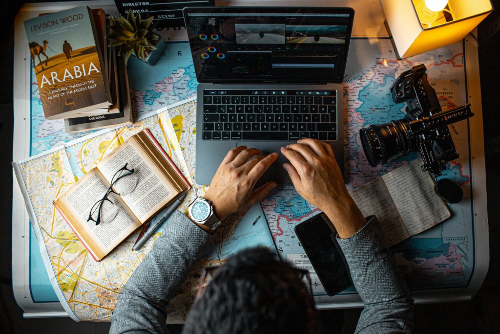 A man with a laptop is shown exploring historical sites with some maps on desk.