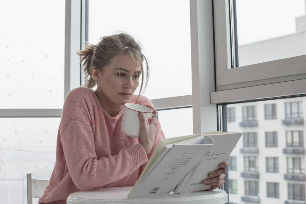 A girl holding cup of coffee and reading book.